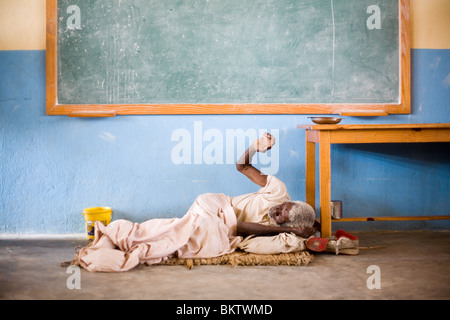 Une personne âgée, malades mentaux homme dort sur le plancher d'une salle de classe après le tremblement de terre de janvier en Haïti. Banque D'Images