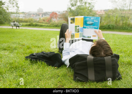 Man lying on lawn la lecture d'un magazine Banque D'Images