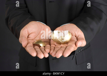 Businessman holding broken golden egg in cupped hand, cropped Banque D'Images