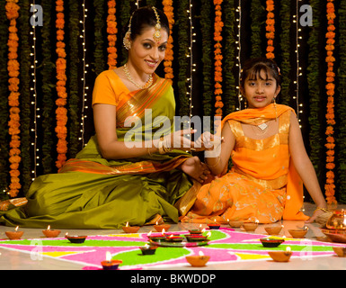 Mère et fille indienne une lampe à huile de l'éclairage en face de rangoli Banque D'Images