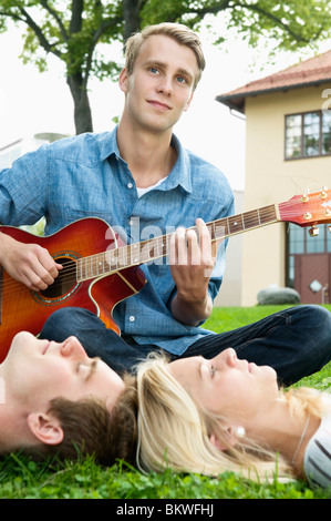 Guy à l'extérieur à jouer de la guitare pour ses camarades de classe Banque D'Images