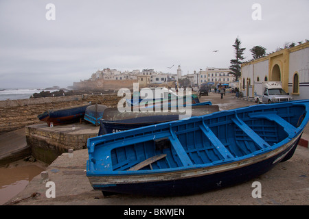 Bateaux de pêche bleu tiré hors de la mer boueuse en route vers le port d'Essaouira avec les murs de la ville et Medina Banque D'Images