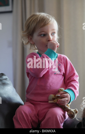 DEUX ANS SUCER LE POUCE : enfant de deux ans bébé fille sucer le pouce assis assis assis assis assis canapé-lit soft jouet tenir le modèle libéré Banque D'Images