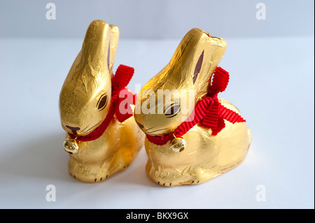 Lapins de pâques en chocolat emballés dans une feuille d'or avec un ruban rouge et une petite cloche Banque D'Images