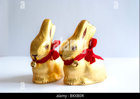 Lapins de pâques en chocolat emballés dans une feuille d'or avec un ruban rouge et une petite cloche Banque D'Images