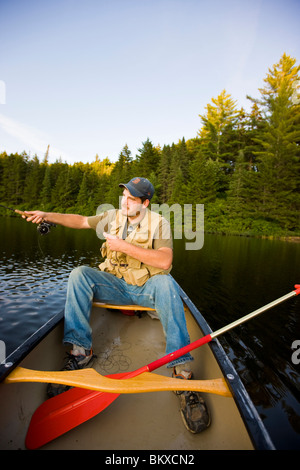 Un homme la voler-pêche à partir d'un canoë sur peu de Greenough étang dans Errol, New Hampshire. Banque D'Images