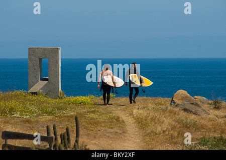Deux hommes portant des combinaisons de surfeurs marchant dans un chemin de terre avec des planches de surf à Punta de Lobos, Pichilemu, Chili.