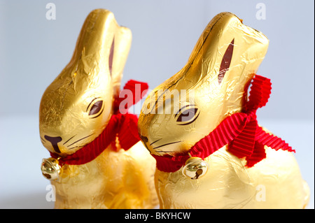 Lapins de pâques en chocolat emballés dans une feuille d'or avec un ruban rouge et une petite cloche Banque D'Images