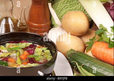 Potage de légumes (soupe minestrone) dans un bol en verre noir, burette d'huile d'olive extra vierge, poivre mil et de légumes de saison bio Banque D'Images