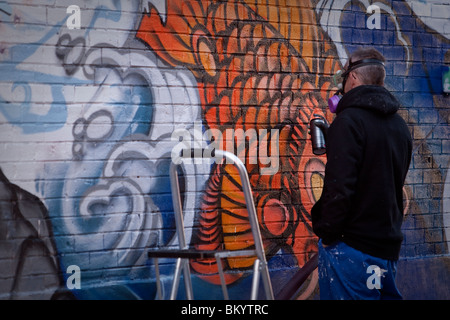 Un graffiti artiste utilise un aérosol de peinture pour créer un morceau à Toronto Banque D'Images