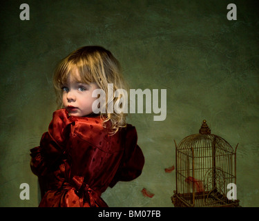 Une jeune fille portant une robe rouge à l'arrière de l'appareil photo à côté d'une cage à oiseaux Banque D'Images