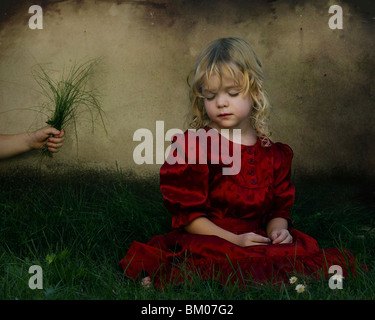 Une jeune fille assise sur l'herbe avec ses yeux fermés et portant une robe de satin rouge Banque D'Images