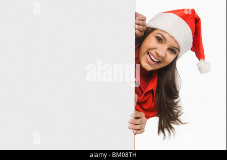 Femme en costume de Père Noël furtivement derrière une porte et souriant Banque D'Images