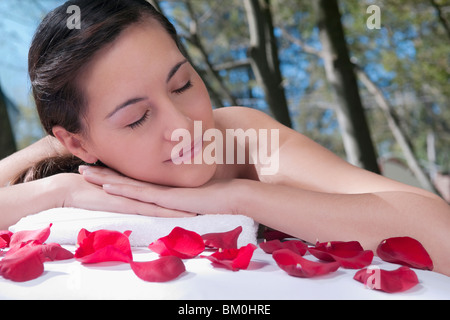 Femme couchée sur une table de massage avec des pétales de rose en face d'elle Banque D'Images