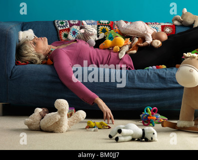 Hauts femme endormie sur un canapé avec des jouets Banque D'Images