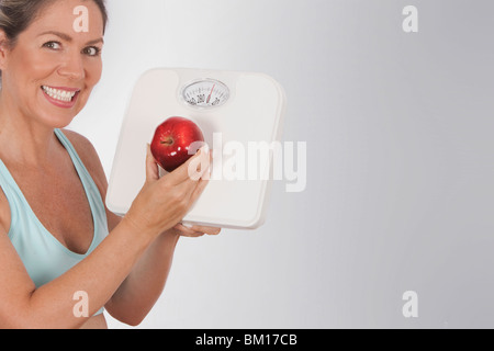 Femme tenant une balance de salle de bains et d'un apple and smiling Banque D'Images