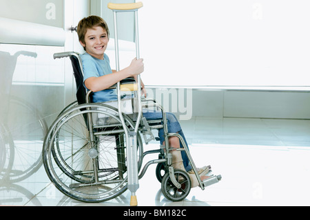 Boy holding béquille et assis dans un fauteuil roulant Banque D'Images