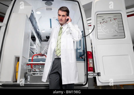 Doctor talking on a mobile phone en face d'une ambulance Banque D'Images