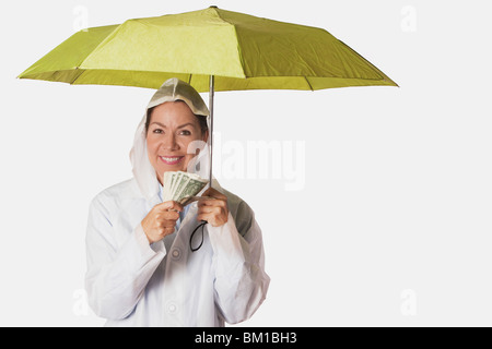 Femme en manteau de pluie s'abritant sous un parapluie et la tenue des notes de devise Banque D'Images