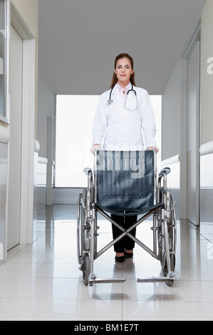 Femme médecin poussant un fauteuil roulant vide Banque D'Images