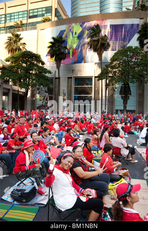 Red-shirted heureux manifestants s'asseoir dans la rue fermé dominé par les grands magasins. Banque D'Images