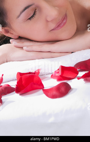 Femme couchée sur une table de massage avec des pétales de rose en face d'elle Banque D'Images