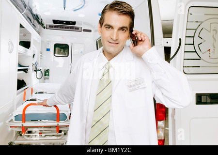 Doctor talking on a mobile phone en face d'une ambulance Banque D'Images