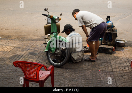 Mécanicien moto routière au travail sur une vieille Honda Cub sur Tran Hung Dao Street à Cholon. Banque D'Images