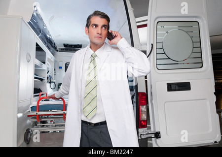 Doctor talking on a mobile phone en face d'une ambulance Banque D'Images