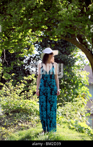 Jeune femme de 20 ans portant un magasin robe de paons avec floppy white hat et lunettes UK Banque D'Images