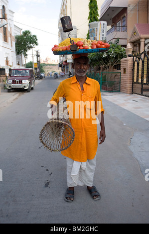 Dans l'homme kurta jaune avec le bac d'en-cas sur sa tête et le tableau sous son bras, pour les vendre au marché, Jodhpur, Rajasthan, India Banque D'Images