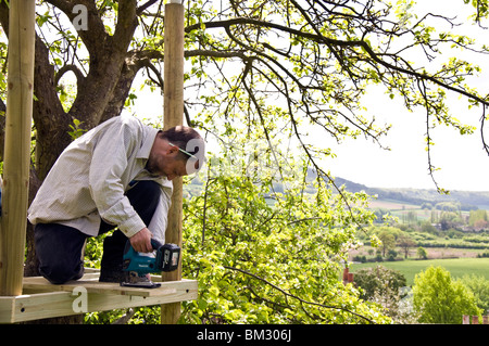 L'homme l'édification d'une cabane autour d'un pommier utilise un outil électrique sans fil Banque D'Images