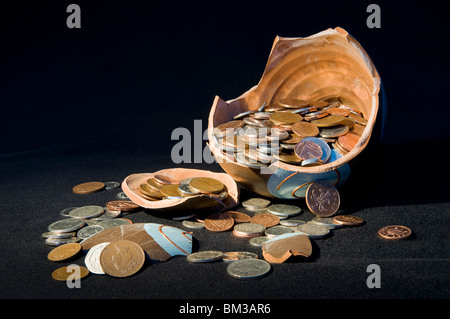 Broken terramundi pot d'épargne avec de l'argent s'échappe au-dessus de la table sur un fond noir Banque D'Images