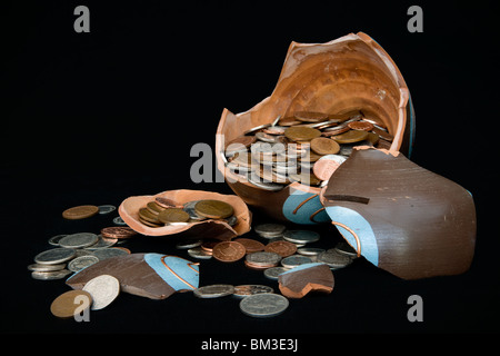 Broken terramundi pot d'épargne avec de l'argent s'échappe au-dessus de la table sur un fond noir Banque D'Images