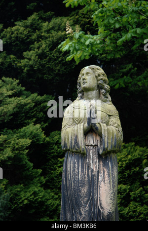 Statue de femme victorienne avec elle les mains jointes en prière sur un fond d'arbres dans le cimetière, doyen d'Édimbourg. Banque D'Images