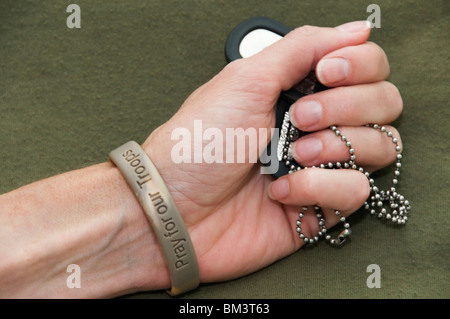 La main de femme est titulaire d'identification militaire 'dog' tags. Elle porte un bracelet avec des mots à l'appui de militaires. Banque D'Images