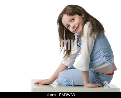 Belle petite fille en bleu vêtements est assis sur une chaise blanche, isolated on white Banque D'Images