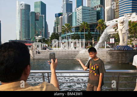 Tourist posant pour une photo devant la statue du Merlion et sur les toits de la ville, l'Esplanade, à Singapour Banque D'Images