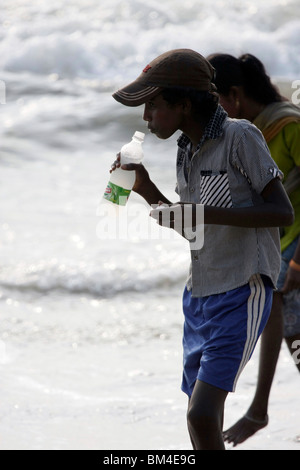 Jeune indien assoiffé de boire des boissons non alcoolisées dans une bouteille en plastique dans la plage, Kerala, Inde Banque D'Images