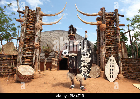 Un homme d'origine tribale zoulou porte des vêtements traditionnels tout en pose avec un ballon de soccer dans un village traditionnel en Afrique du Sud Banque D'Images