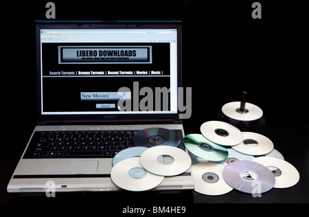 Site de téléchargement illégal et bittorrent site sur un ordinateur à côté d'une pile de copies de DVD. Banque D'Images