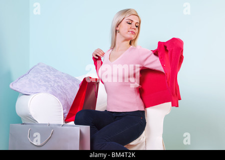 Une belle femme blonde assis sur une chaise d'essayer sur de nouveaux vêtements qu'elle vient d'acheter. Banque D'Images