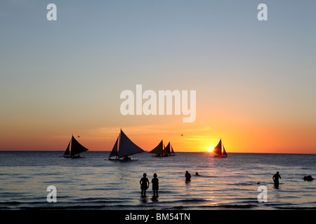 Voiliers sillonnent la rive au coucher du soleil sur la plage Blanche, Boracay, la plus célèbre destination touristique aux Philippines. Banque D'Images