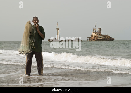 L'homme de la pêche au filet à partir de la rive en face d'un naufrage, Palmarin, Sénégal, Afrique. Banque D'Images