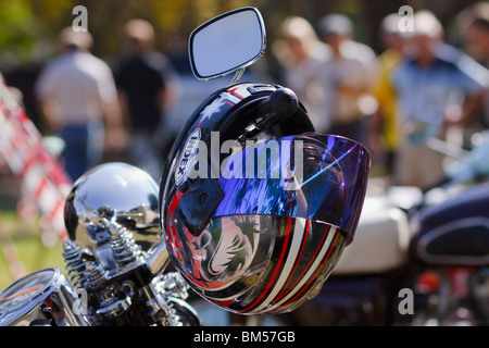 Casque colorés drapés sur le guidon d'une moto. Les gens méconnaissables en arrière-plan de netteté. L'accent de premier plan. Banque D'Images