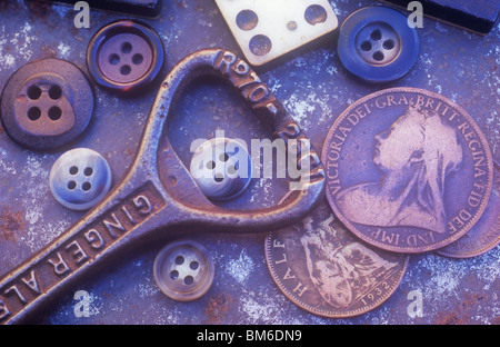 Ancien décapsuleur avec pièces domino homme boutons et trois vieux British coins couché sur le plateau métallique rouille Banque D'Images