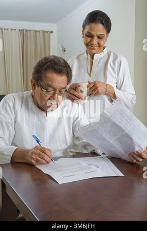 L'homme faire le tri des factures avec une femme à boire le thé à côté de lui Banque D'Images