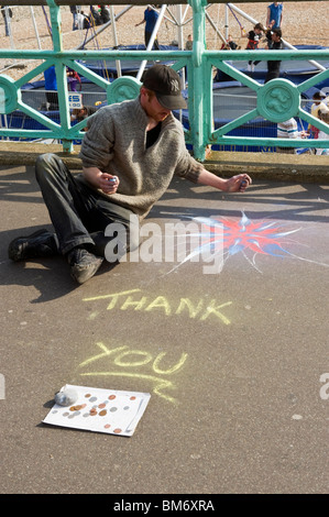 Un artiste de rue de la chaussée à l'aide de craies de couleur pour créer un dessin à la craie, à Brighton. Banque D'Images