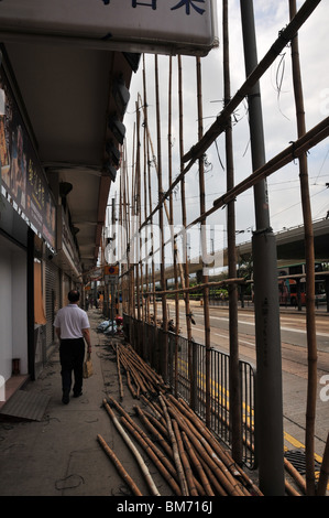 Homme marchant sur un trottoir en face de magasins avec des échafaudages en bambou, Connaught Road West, Sheung Wan, Hong Kong Banque D'Images