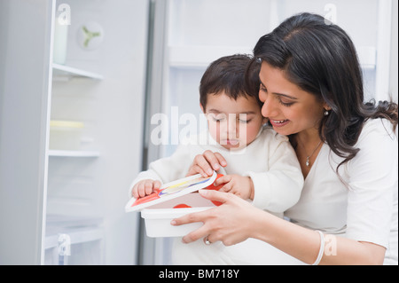 Baby Boy mettre les tomates dans un récipient avec sa mère Banque D'Images